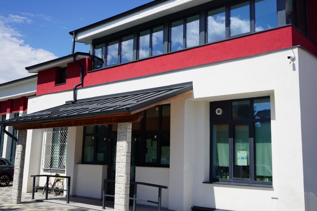 Modern two-story building with red and white facade, large windows, and a covered entrance; bicycle parked outside.