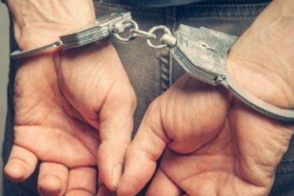 Person with hands cuffed behind their back, wearing metal restraints connected by a chain behind them