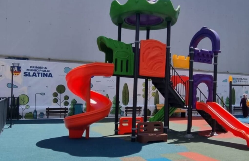 Colorful playground structure with red spiral slide, green and purple ramps, and a bright red straight slide in a sunny outdoor park area.