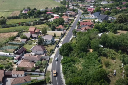 Aerial view of a rural town with a curving road running between houses and green fields on either side.