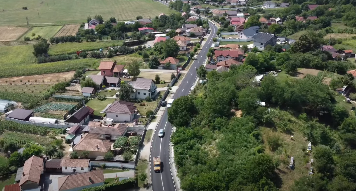Aerial view of a rural town with a curving road running between houses and green fields on either side.