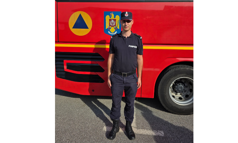Firefighter in a black uniform standing in front of a red fire truck with blue emblem and yellow triangle symbol.