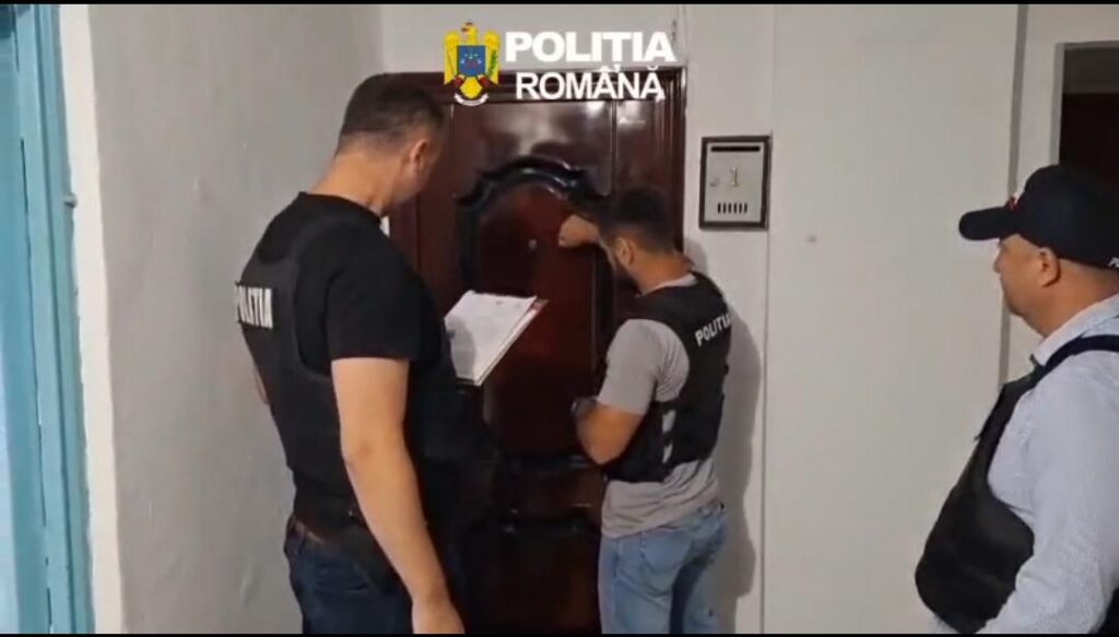 WhatsApp Image 2026-07-02 at 143530 - Jurnalul Olteniei – Știri din Craiova și Oltenia Three Romanian police officers in tactical vests inspect a large wooden armoire in a hallway, one holding a clipboard.