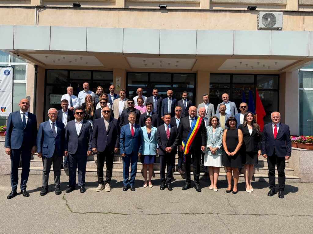 Large group of professionals in business attire posing on building steps, with a Romanian flag in the background.