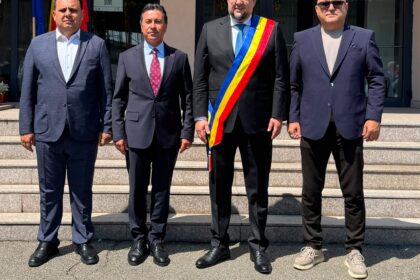 Four men in suits pose on stone steps outside a building; the third man wears a blue-yellow-red ceremonial sash.