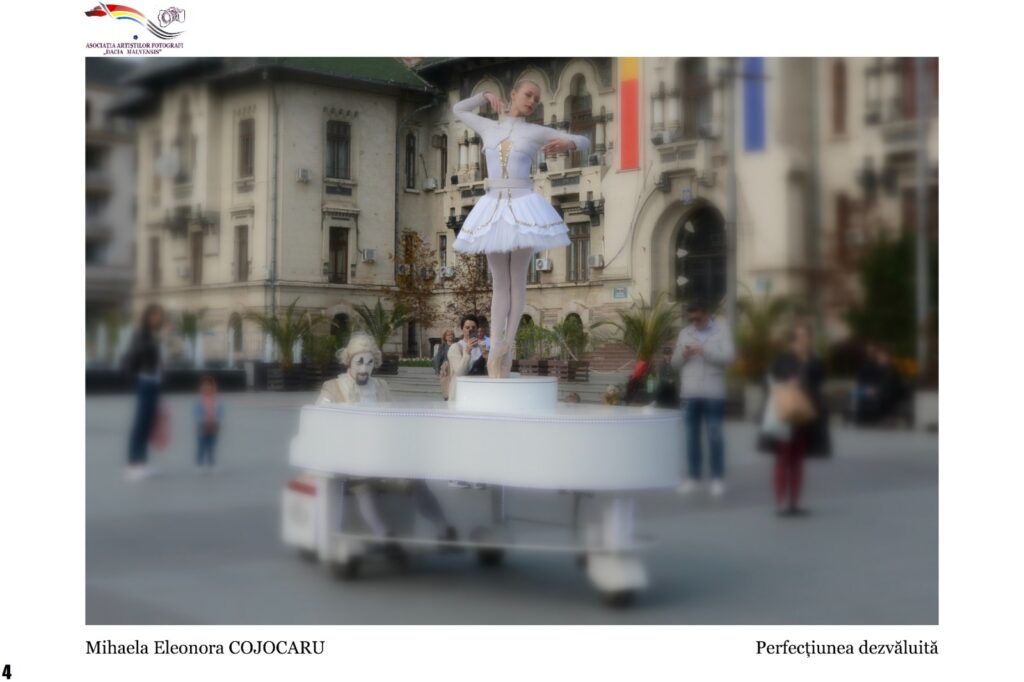Ballerina in a white tutu standing on a white platform piano in a city square, with onlookers and historic buildings in the background.