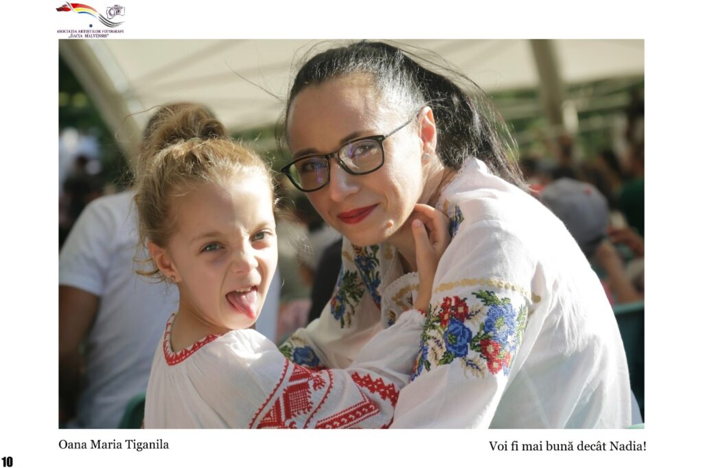 Two women in traditional embroidered blouses hug and smile outdoors; the woman on the right wears glasses.