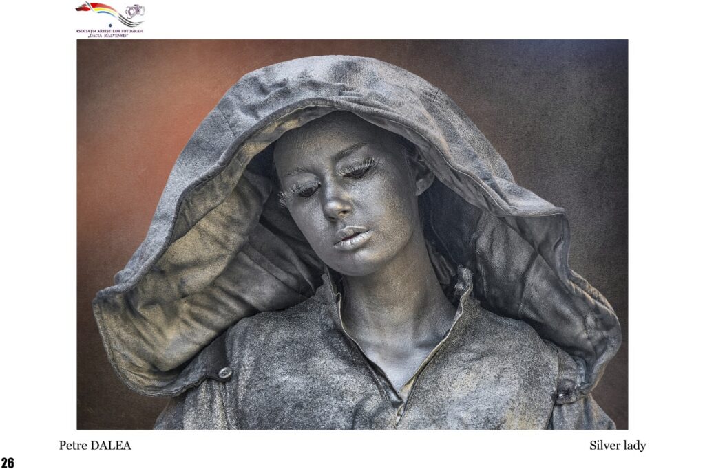 Gray-toned statue of a woman with a large hooded cloak, serene expression; sculpture titled 'Silver Lady' by Petre Dălea.