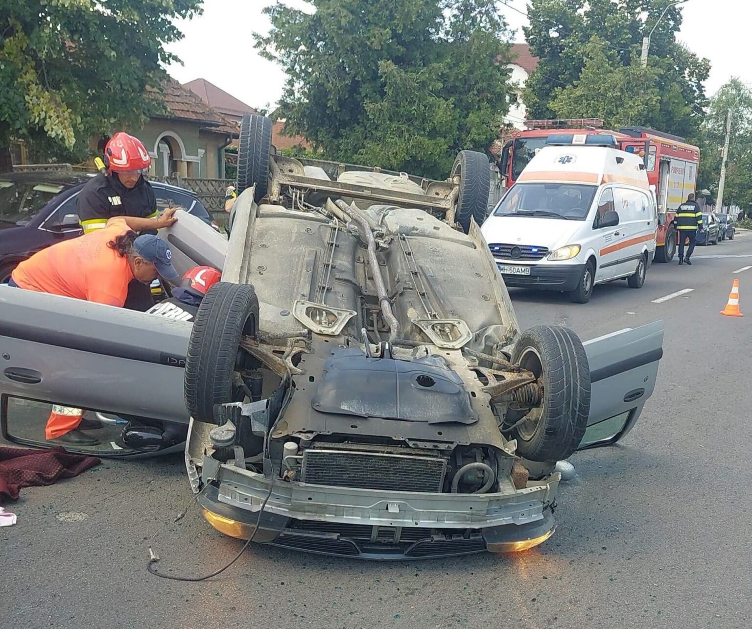 Accident la Strehaia: șofer transportat la spital după impact - Jurnalul Olteniei – Știri din Craiova și Oltenia Emergency responders attend to a overturned car on a residential street; ambulance and fire truck parked nearby.