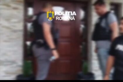 Blurry image of Romanian police officers at a doorway, with the Politia Romana logo visible above them.