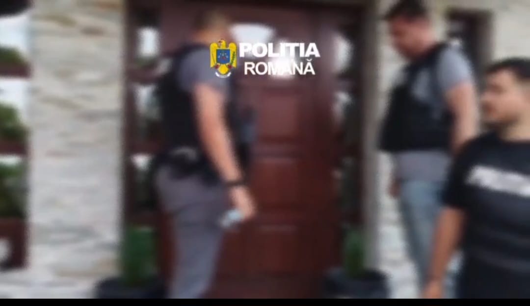 Blurry image of Romanian police officers at a doorway, with the Politia Romana logo visible above them.