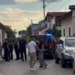 Group of police officers and civilians stand on a residential street beside a police SUV with blue lights on.