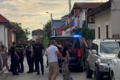 Group of police officers and civilians stand on a residential street beside a police SUV with blue lights on.