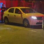 Nighttime street scene with a white hatchback and a police car, with three officers standing nearby.