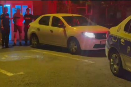 Nighttime street scene with a white hatchback and a police car, with three officers standing nearby.
