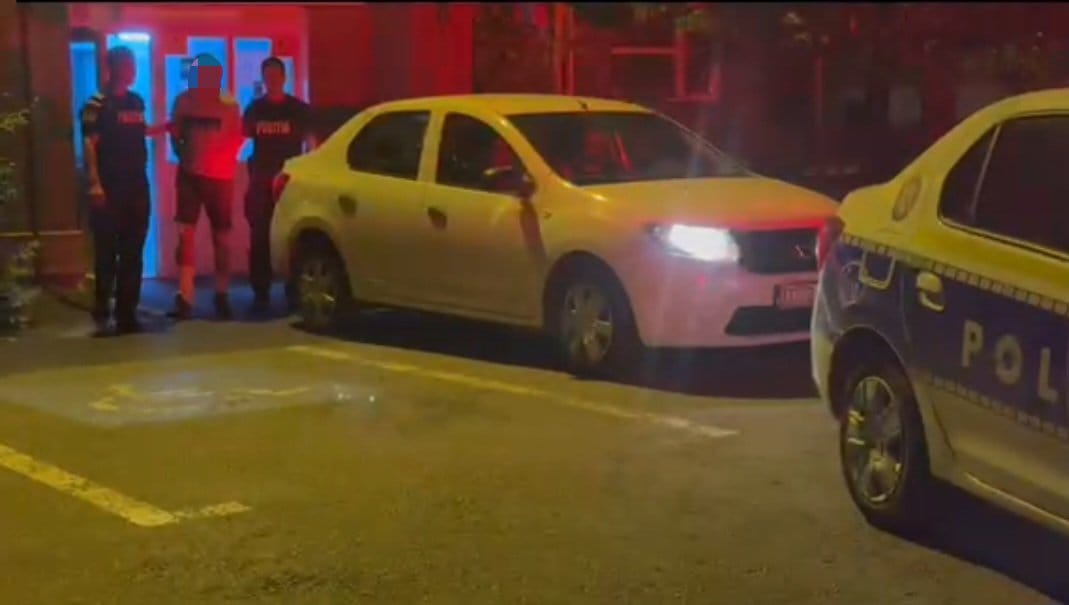 Reținut în Craiova după ce a încălcat ordinul de protecție - Jurnalul Olteniei – Știri din Craiova și Oltenia Nighttime street scene with a white hatchback and a police car, with three officers standing nearby.