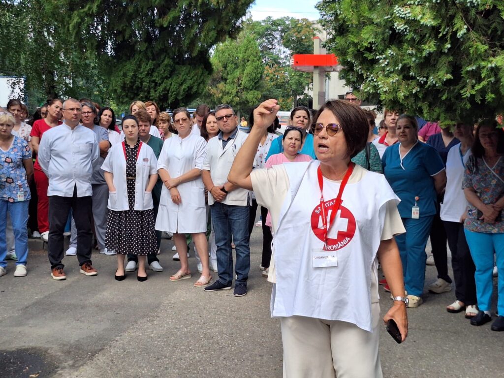 WhatsApp Image 2026-07-20 at 110651 - Jurnalul Olteniei – Știri din Craiova și Oltenia Group of healthcare workers gathered outdoors, a woman in front raising her hand and speaking to the crowd.