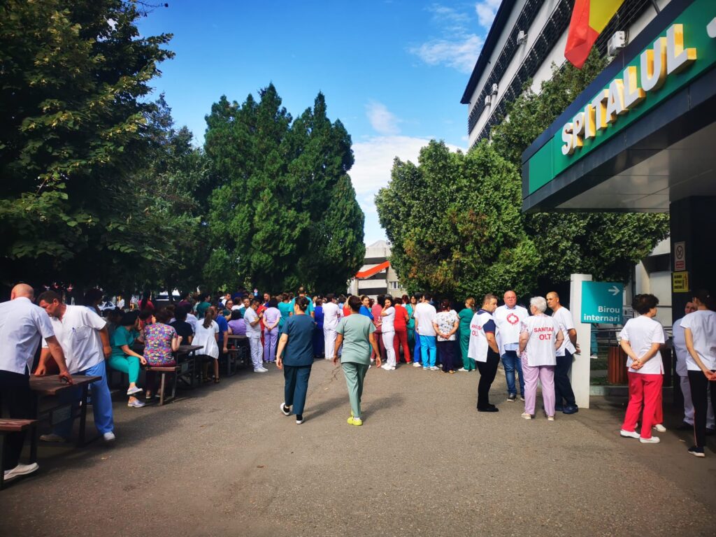 WhatsApp Image 2026-07-20 at 110756 1 - Jurnalul Olteniei – Știri din Craiova și Oltenia Large crowd of medical staff and visitors gathered outside a hospital entrance under a clear blue sky.
