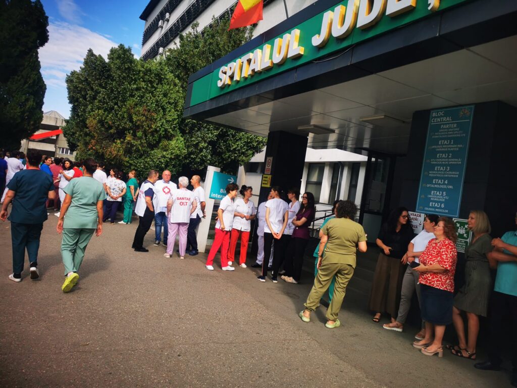 WhatsApp Image 2026-07-20 at 110756 - Jurnalul Olteniei – Știri din Craiova și Oltenia Group of healthcare workers in scrubs and uniforms gathered outside a hospital entrance.