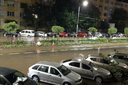 Nighttime street scene with a flooded road and parked cars along the curb; water covers the roadway in a city