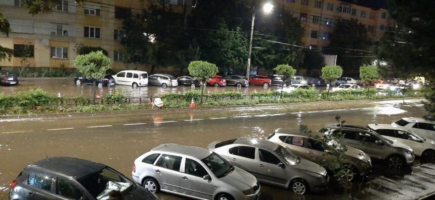 Nighttime street scene with a flooded road and parked cars along the curb; water covers the roadway in a city