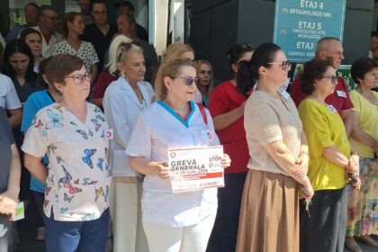 A diverse crowd of healthcare workers and civilians standing outdoors near a hospital entrance, some wearing scrubs and badges.