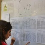 Woman with long dark hair reads a wall of printed schedules pinned to a bulletin board.