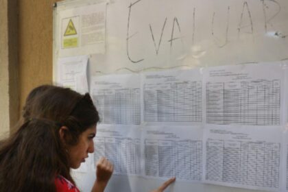 Woman with long dark hair reads a wall of printed schedules pinned to a bulletin board.