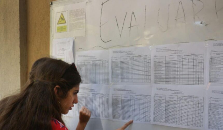 Woman with long dark hair reads a wall of printed schedules pinned to a bulletin board.