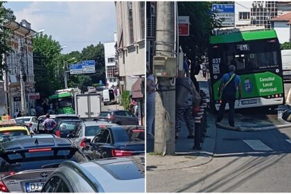 Busy urban street filled with cars, taxis, and a green municipal bus ahead in heavy traffic at a sunny day location with buildings lining the road and people nearby on the sidewalk.