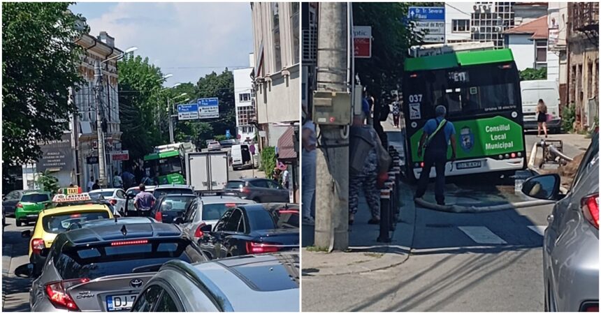 Busy urban street filled with cars, taxis, and a green municipal bus ahead in heavy traffic at a sunny day location with buildings lining the road and people nearby on the sidewalk.