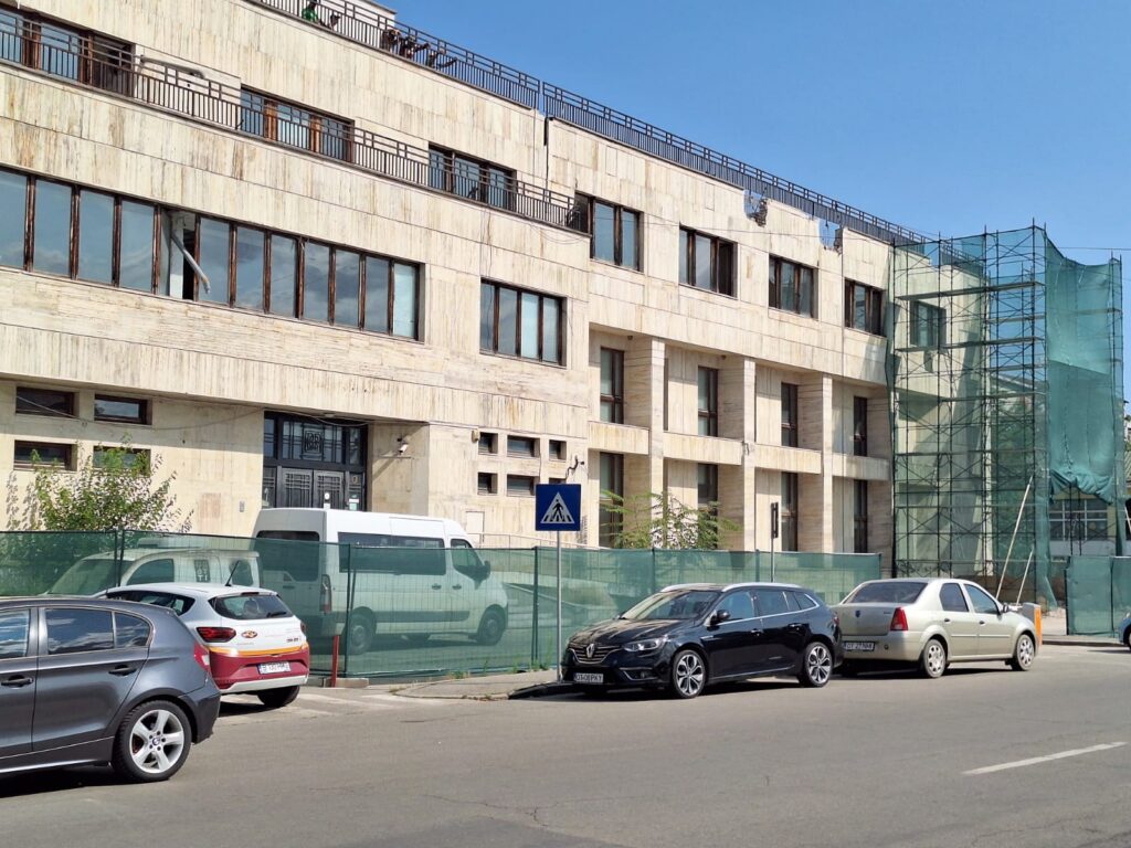 bcr slatina victoria intermed 5 - Jurnalul Olteniei – Știri din Craiova și Oltenia Beige stone building under construction with scaffolding on the right and parked cars along the street under a blue sky