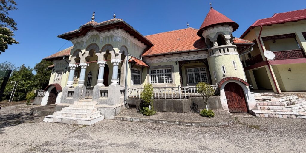 conacul romano plesoiu 1 - Jurnalul Olteniei – Știri din Craiova și Oltenia Historic villa with arched colonnade, decorative capitals and a round turret with a red cone roof against a blue sky.