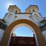 Front view of a decorative arched gateway with two towers, white walls and terracotta trim against a clear blue sky