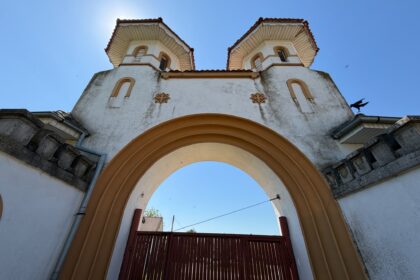 Front view of a decorative arched gateway with two towers, white walls and terracotta trim against a clear blue sky