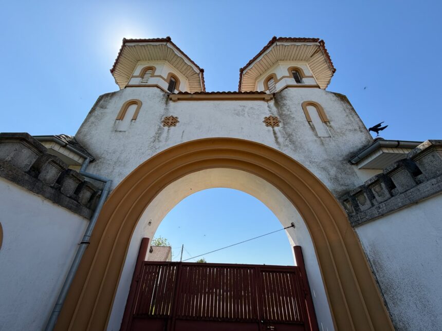 Front view of a decorative arched gateway with two towers, white walls and terracotta trim against a clear blue sky