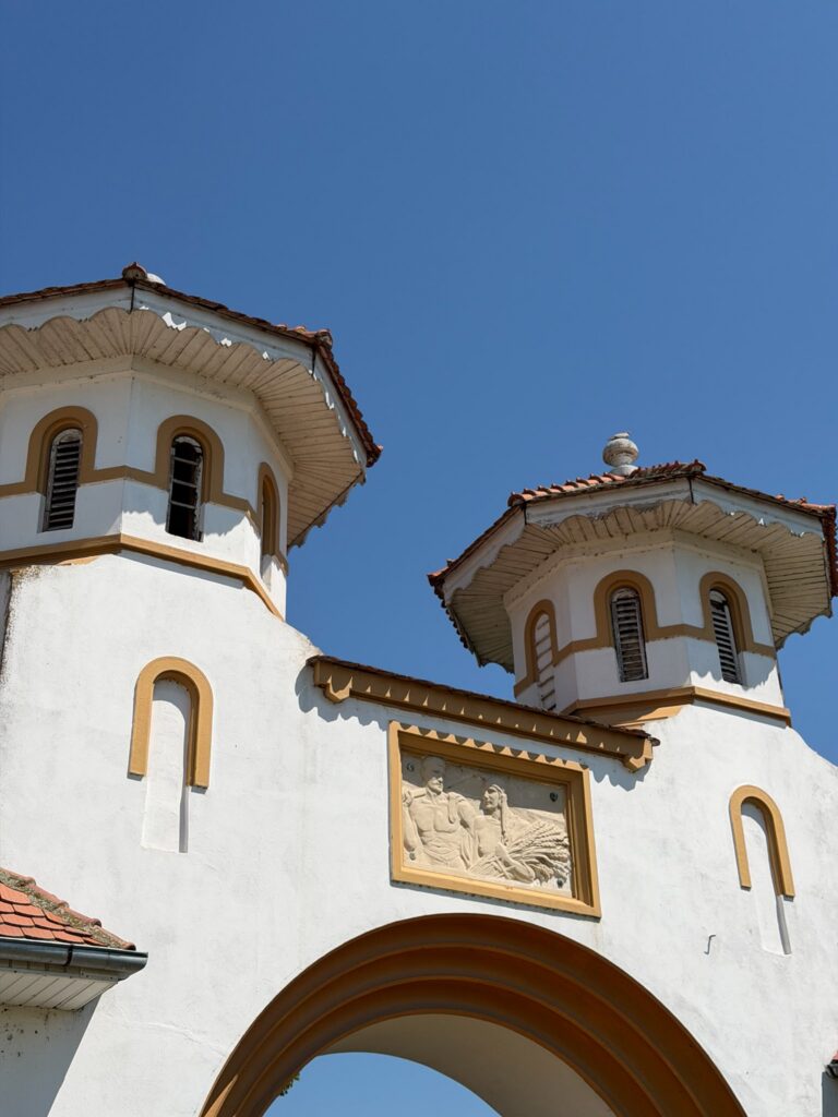 conacul romano plesoiu 11 - Jurnalul Olteniei – Știri din Craiova și Oltenia White church facade with arched windows and orange trim, two cupola towers under a clear blue sky.