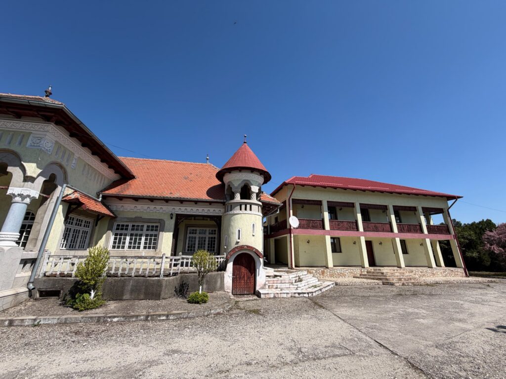 conacul romano plesoiu 4 - Jurnalul Olteniei – Știri din Craiova și Oltenia Historic building with red tiled roof and ornate plasterwork against a clear blue sky, featuring a small turret at the corner and arched windows.