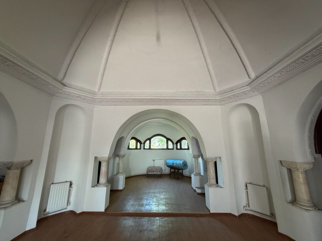 conacul romano plesoiu 5 - Jurnalul Olteniei – Știri din Craiova și Oltenia Interior of a bright white church hall with arches, decorative molding, and marble columns leading to a row of arched windows at the far end.