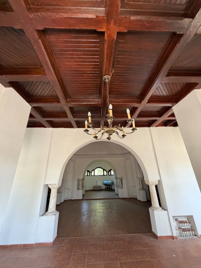 conacul romano plesoiu 7 - Jurnalul Olteniei – Știri din Craiova și Oltenia Interior of a room with a dark wood coffered ceiling and a brass chandelier hanging from a chain over a tiled floor.