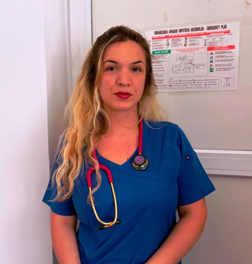 doctorita sju - Jurnalul Olteniei – Știri din Craiova și Oltenia Female healthcare worker in blue scrubs with a stethoscope around her neck, standing beside an emergency plan poster.