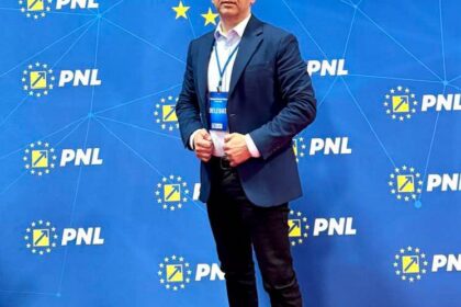Man in a dark suit posing on a red carpet in front of a blue PNL backdrop with EU stars and a badge visible on his chest.