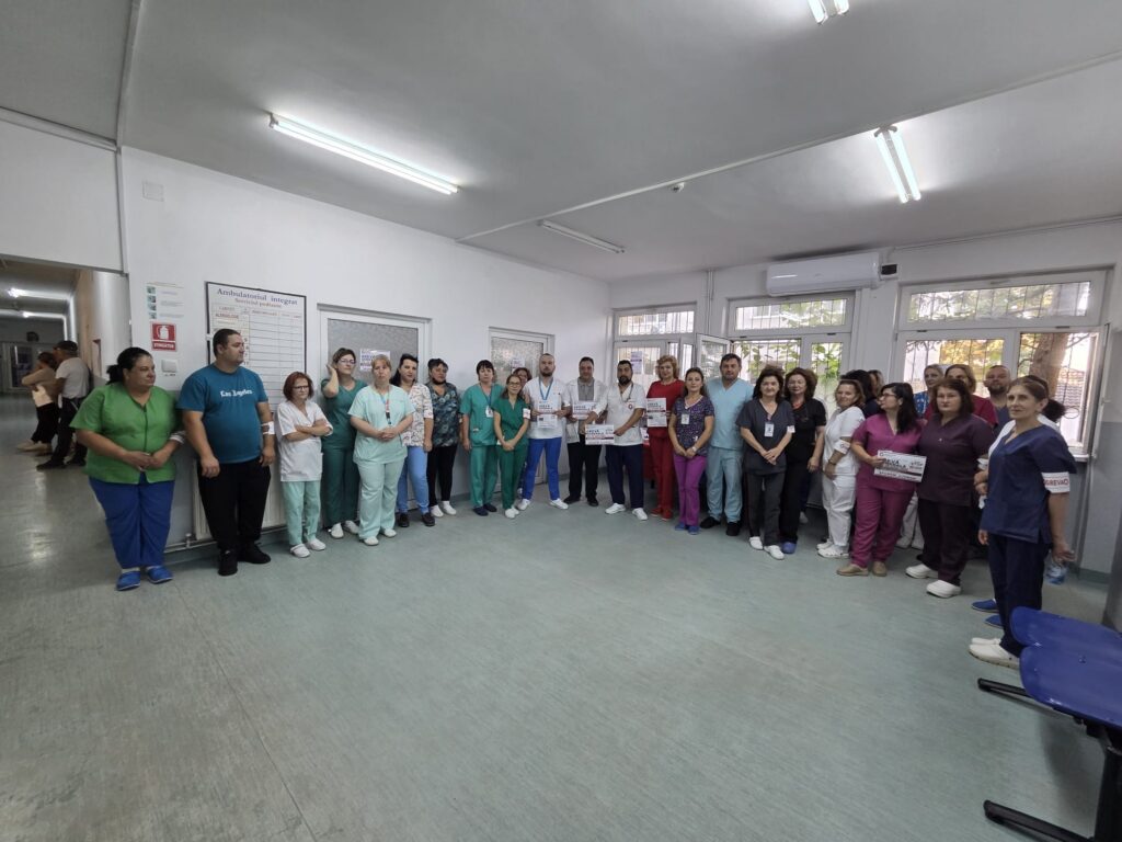 Group of healthcare workers and staff posing in a hospital hallway or ward.