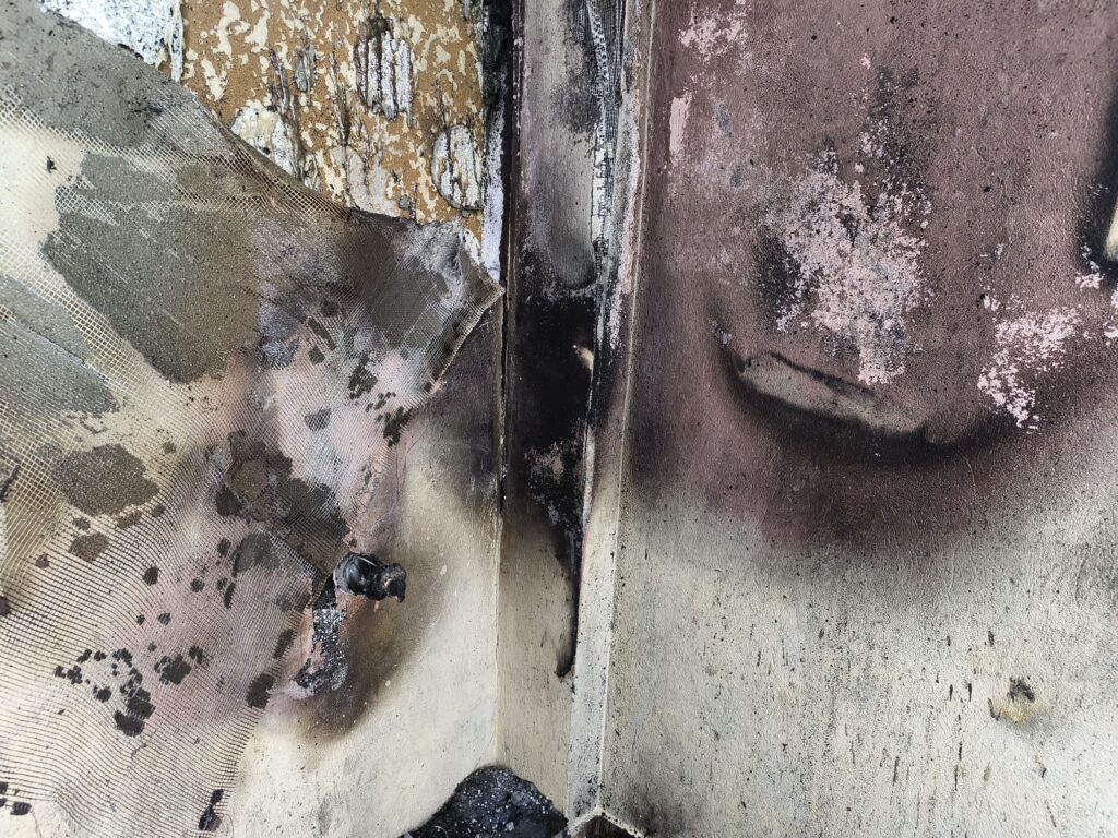 incendiu piatra Olt 1 - Jurnalul Olteniei – Știri din Craiova și Oltenia Close-up of a soot-covered wall with peeling paint, exposed mesh, and charred debris along a seam.