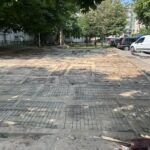 Parking lot under renovation with a web of steel rebar on the ground, trees along the edges, and parked cars on the right.