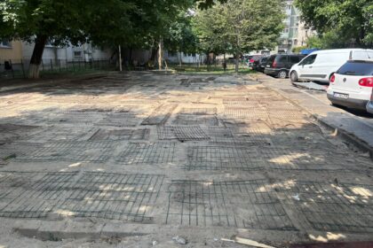 Parking lot under renovation with a web of steel rebar on the ground, trees along the edges, and parked cars on the right.