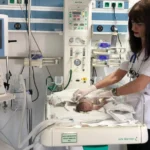 Nurse in a white uniform tending to a newborn in an incubator in a hospital NICU.