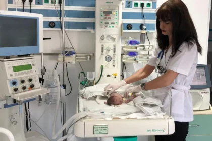 Nurse in a white uniform tending to a newborn in an incubator in a hospital NICU.