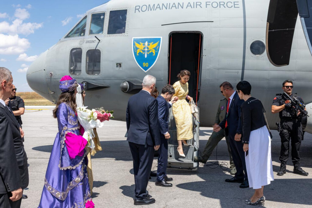 A woman in a yellow dress steps down a military jet while officials and security stand nearby at an airfield.