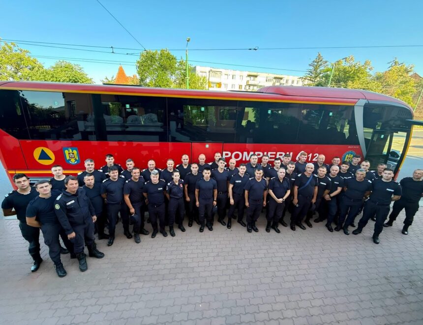 Group of uniformed firefighters posing in front of a red rescue bus labeled 'POMPIERII' on a sunny day.